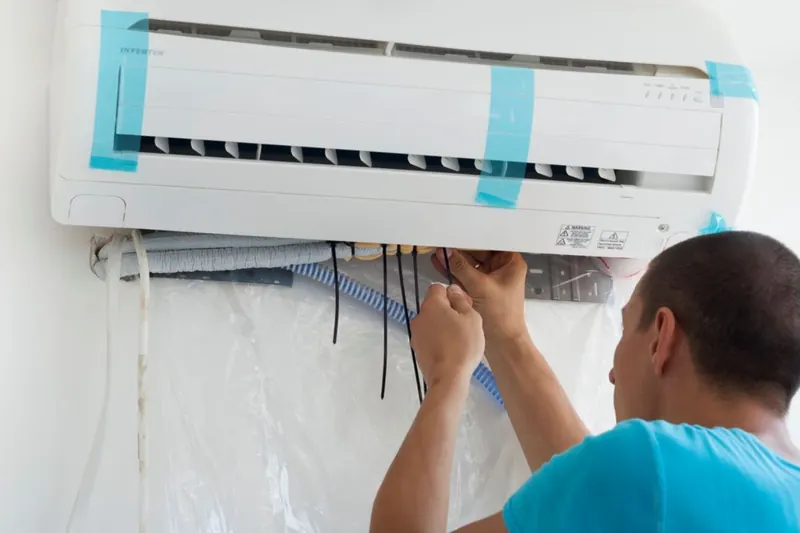 Technician connecting the wiring and pipes of a new wall-mounted split air conditioner